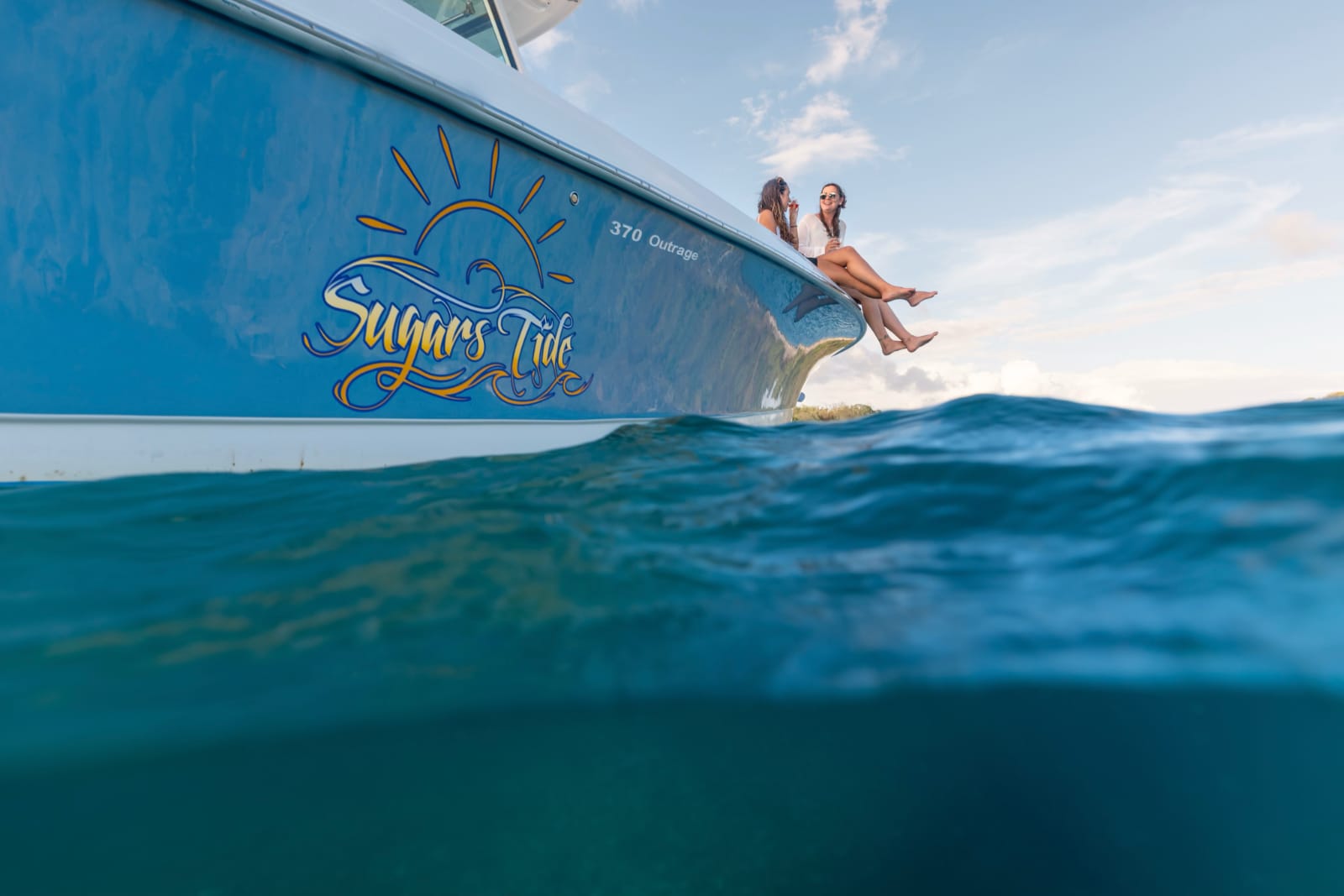 Two people sitting on private charter boat with legs hanging in water